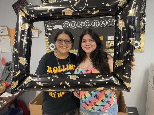 Two female student smiling holding a graduation frame